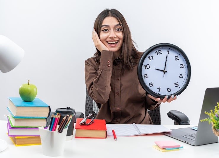 excited-young-school-woman sits table-with school tools holding wall clock putting hand cheek