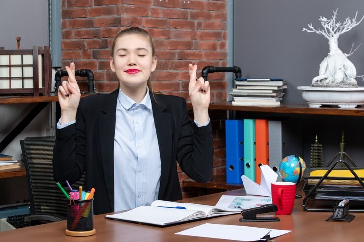 top view smiling young female sitting table holding document crossing her fingers dreaming about something office